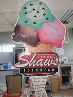 Full view of the Shaw's Ice Cream advertising sign showing three colorful scoops of ice cream and cone with the established year text.
