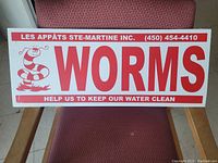 Front view of the corrugated plastic worm sign showing red lettering and cartoon worm on white background, placed on a red chair.