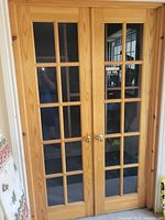 Front view of two pine French doors with multiple glass panes and brass knobs, showing condition and attached hinges.
