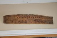 Front view of rustic live edge wood slab sign displaying "Welcome To The Other Room" in cursive script.