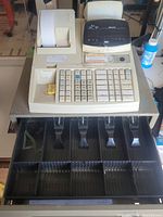 Front angled view showing the numeric keypad, receipt printer, cash drawer open with compartments for bills and coins, and the key inserted.
