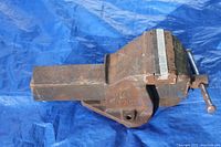 Photo of the vintage Record No 6 mechanics vise on blue tarp, showing heavy rust and wear on the cast iron body with the screw handle for adjusting the jaws.