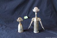 Front view of the two zinc figures, the smaller bell and the taller cork screw, showing humanoid features and metallic patina.