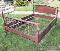 Full view of antique spindle double bed frame outside on grass, showing headboard, footboard, side rails, and turned spindle posts.