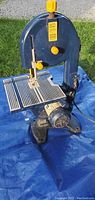 Band saw on blue tarp outdoors, showing entire tool from front with motor base and work table