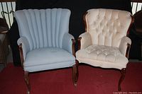 Both chairs side by side on red carpet with black backdrop; beige tufted back armchair on right and blue channel back chair on left.