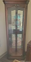 Front view of the corner curio cabinet showing glass doors and carved wood accents on top and bottom front.