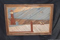 Full view of rectangular framed folk art wooden lathe artwork depicting a lighthouse, dock, boat, and birds in a nautical scene.