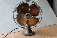 Front view of antique brass oscillating fan showing four brass blades and wire cage.