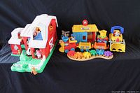 Fisher Price Little People farm barn with figures, Fisher Price train station set, bulldozer, and helicopter toys arranged