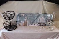 Wide view of the nautical picture, double fruit basket, and oil lamp placed on a white cloth background