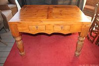 Full view of vintage solid pine butcherblock table with two drawers on red carpet.