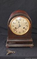 Front view of antique wooden mantel clock with glass face, Arabic numerals, and visible winding key.