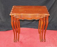 Photo showing three reddish-brown wooden nesting tables stacked together on a red carpet, with visible scratches and wear on surfaces.