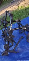 Black metal Thule bike rack for 3 bikes placed on blue tarp outdoors, showing adjustable arms and clamps with rubber pads.