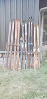 Full set of seven pairs of vintage cross country skis and ski poles arranged against wall outside
