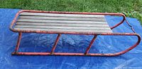 Side view of the vintage sled showing red metal frame with rust and wood slats on top.