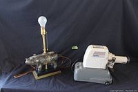 Photo showing Apollo Lumen V-25 slide projector and Alfaraz mid-century pottery rhino lamp with bulb and base on black background.
