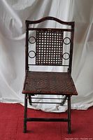 Front view of the wicker folding chair showing the rectangular woven wicker backrest with circular cutouts and damaged wicker seat.
