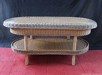 Front view of the wicker coffee table showing the oval top surface and bottom shelf with four support legs.
