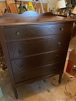 Front view of the antique wooden dresser showing carved drawer fronts, metal handles, and wheels on the legs.