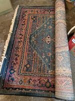 Partially unrolled view of the Gabbeh area rug showing the intricate multi-color design with borders and central patterned medallion.