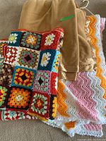Three blankets visible including a beige fleece Berkshire blanket, a multicolored granny square crochet afghan, and a zigzag pink, orange and white crochet afghan.