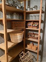 Shelf with multiple clear glass canning jars, wooden baskets, large bushel basket, and wooden wine rack visible