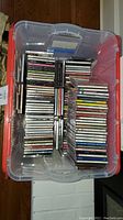 Top-down view of plastic storage bin filled with a large collection of compact discs in standard jewel cases, stacked tightly.