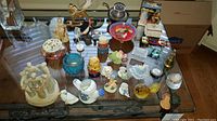 Full view of collection on glass table showing ceramic, porcelain, glass, and metal items including nesting dolls