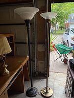 Pair of floor lamps shown side by side with visible bases and glass shades, room background.