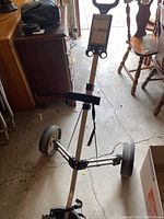 Full view of the 3-wheel golf trolley standing upright on a concrete floor near furniture.