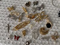 Overview of all pins and brooches laid out on a textured white fabric showing variety of designs and materials