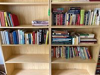 Wooden bookshelf with multiple shelves holding a variety of books in good condition, some larger books stacked horizontally.