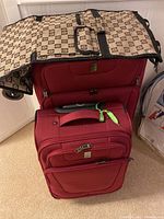 Two red Travelpro suitcases stacked with beige and brown patterned garment bag draped over them.