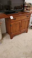 Wooden media cabinet with a TV on top, two side panels folded out on each side demonstrating extension.