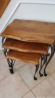 Set of three wooden nesting tables with metal legs stacked underneath each other showing the wood finish and leg design.