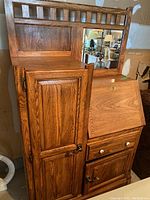 Full view of the oak side cabinet showing door, drawers, drop-down desk surface, and mirror above.