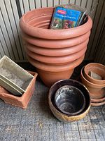 Wide view of multiple outdoor pots including large ribbed terra cotta and clay basket texture pots with two rectangular grey resin pots inside basket pot