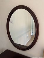 Oval mirror with mahogany wood frame mounted on a wall.