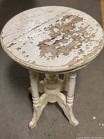 Close-up of round table top showing peeling cream/white paint and a visible large crack.