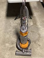 Full front view of Dyson DC 25 vacuum cleaner showing the handle, dust bin, and hose wrapped around the base on a concrete floor.