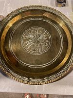 Full view of large round brass wall hanging showing decorative hammered-edge border and etched central design featuring a peacock.