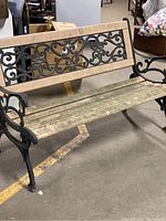 Full front and side view of the garden bench showing metal armrests, decorative metal backrest and slatted plastic seat and backrest, and dirt/weathering on plastic slats.