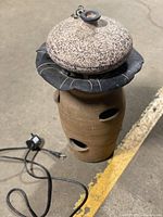 Image showing the garden water fountain fully stacked with electrical cord and pump visible on the ground next to it. The fountain has a beige and dark gray resin finish with a rounded lid on top.
