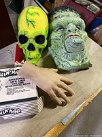 Frankenstein head, neon yellow skull, and life-size beige mechanical hand on a table.