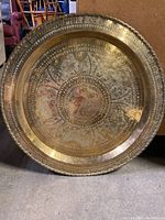Full view of one large round brass wall hanging with intricate hammered and etched floral and geometric designs.