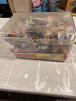 Side view of clear plastic sewing box showing compartments and contents inside