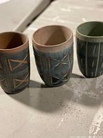 Three pottery cups displayed on a table showing their size and different colors.