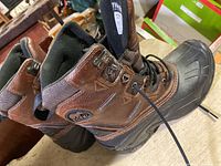 Side view of one brown and black Sorel winter boot showing leather and synthetic upper, laces, and part of the sole.